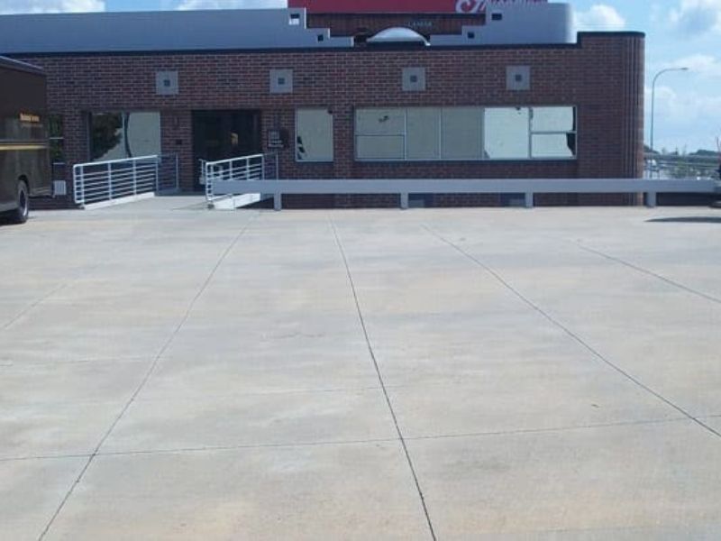 Building entrance with concrete parking area, handrails, and brick walls