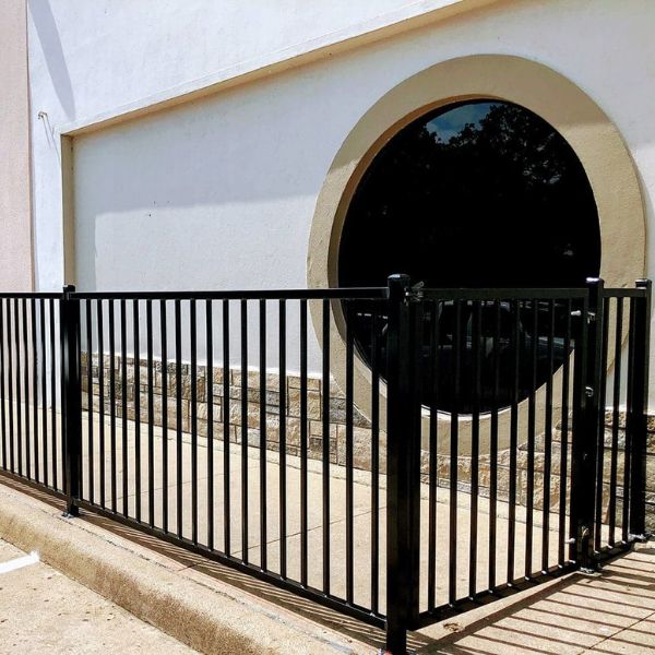 Black Iron fence with vertical bars and gate in front of building with circular window, stone base, and concrete sidewalk