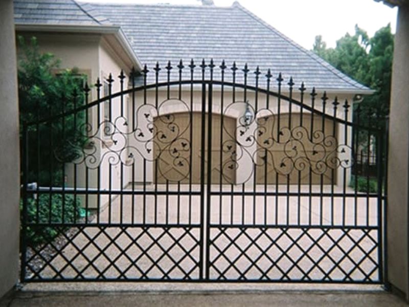Wrought iron driveway gate with scrollwork in front of a residential garage