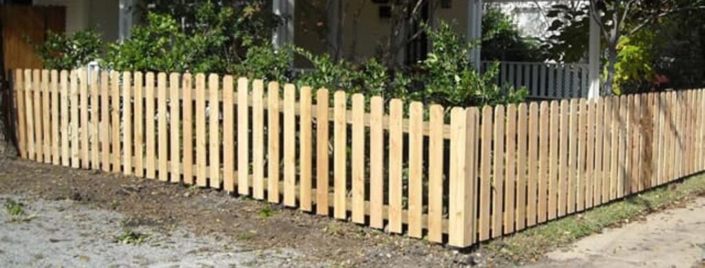 New wooden picket fence enclosing a garden with green plants and shrubs